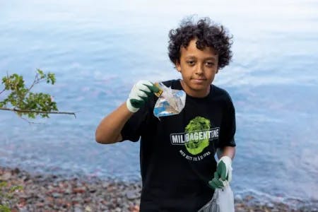 En miljøagent står i strandkanten og plukker søppel. Han viser frem søppel han har funnet, i den andre hånden holder han en søppelpose.