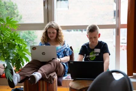 En jente og en gutt sitter foran et vindu med laptop og skriver rapport basert på innspill om klima og miljø fra barn i hele Norge