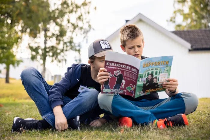 To gutter sitter på gresset og leser bladet Miljøagentrapporten sammen