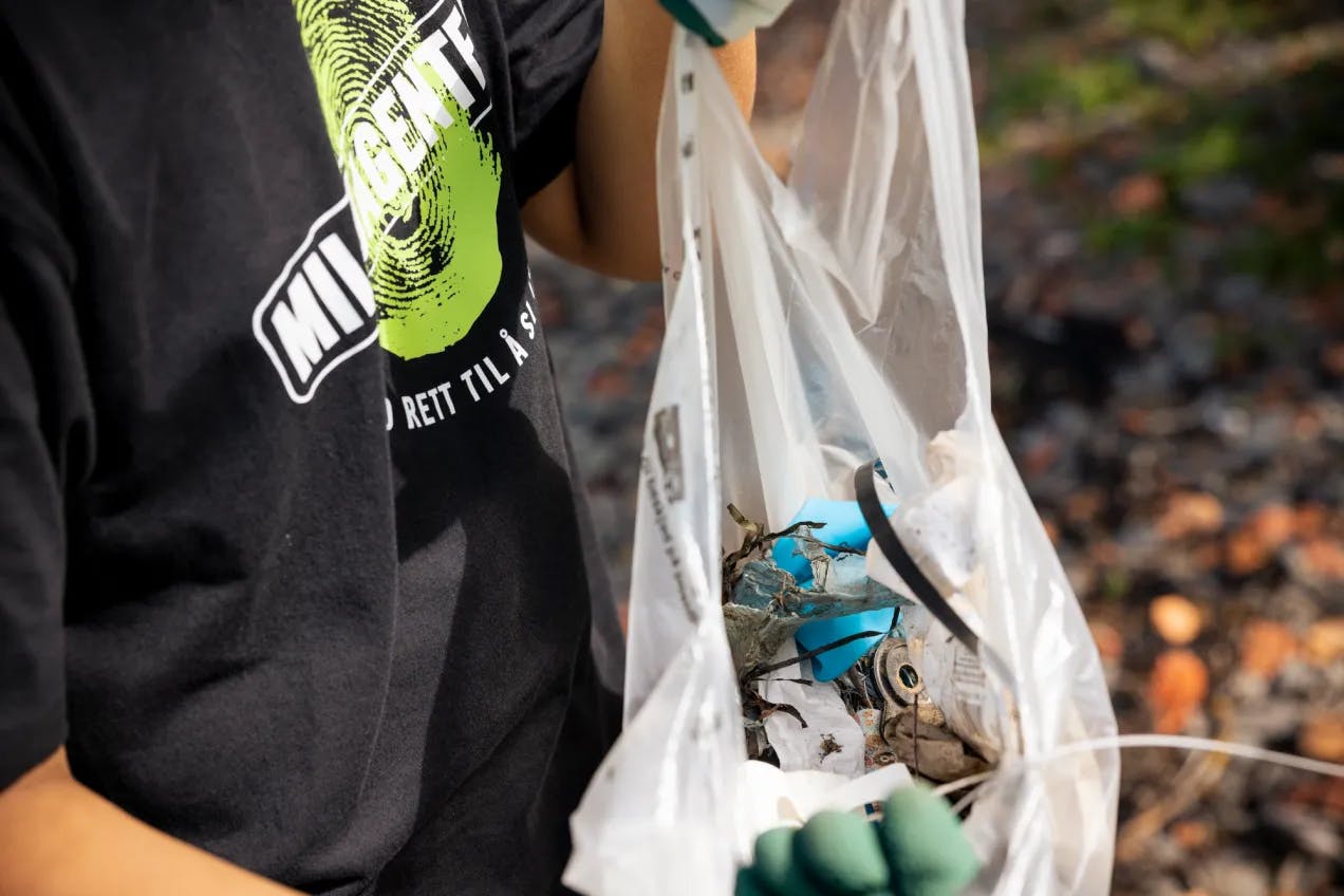 miljøagent holder en hvit plastpose med diverse søppel oppi