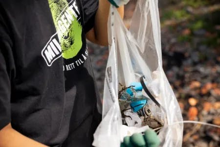 miljøagent holder en hvit plastpose med diverse søppel oppi